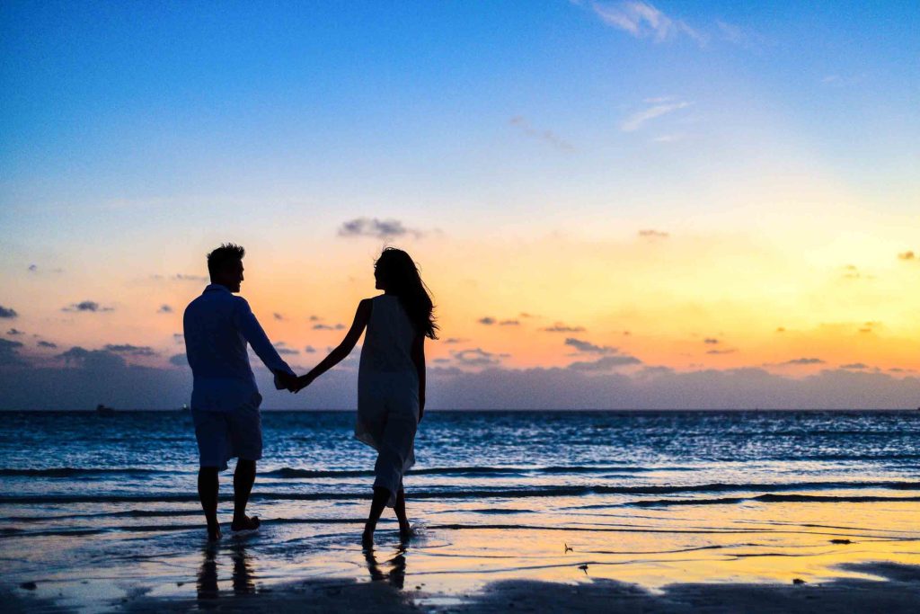 A couple holding hands on the beach at sunset, enjoying a romantic moment together amidst the beautiful scenery.