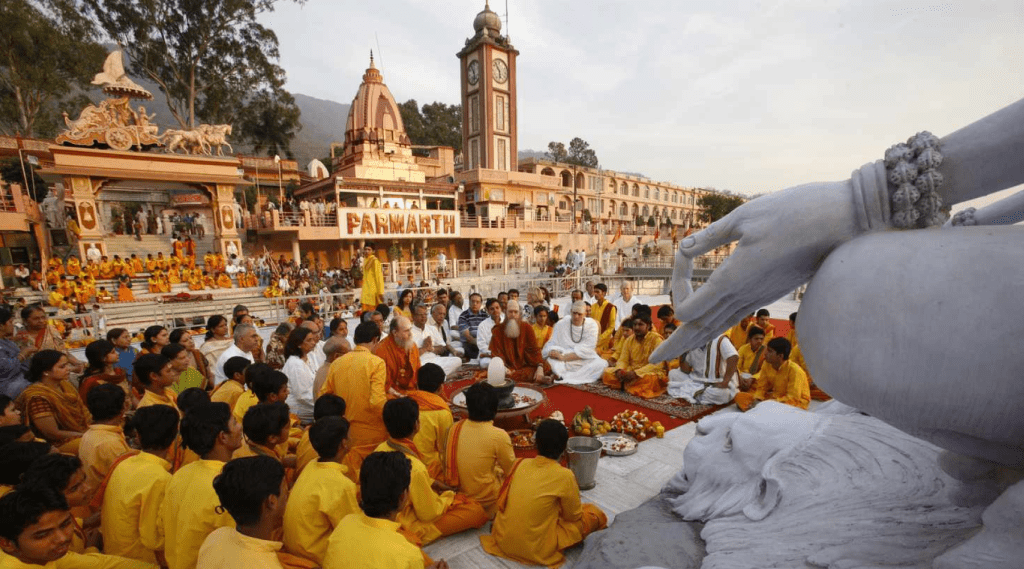 A gathering of individuals in yellow robes seated around a statue in a Ashram.