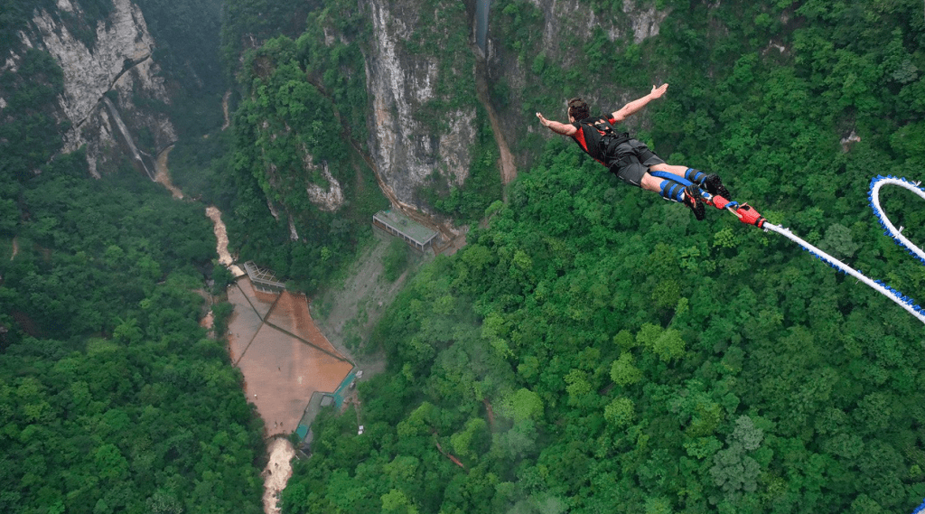 A man soaring through the air after jumping off a rope enjoying Bunjee jumping.
