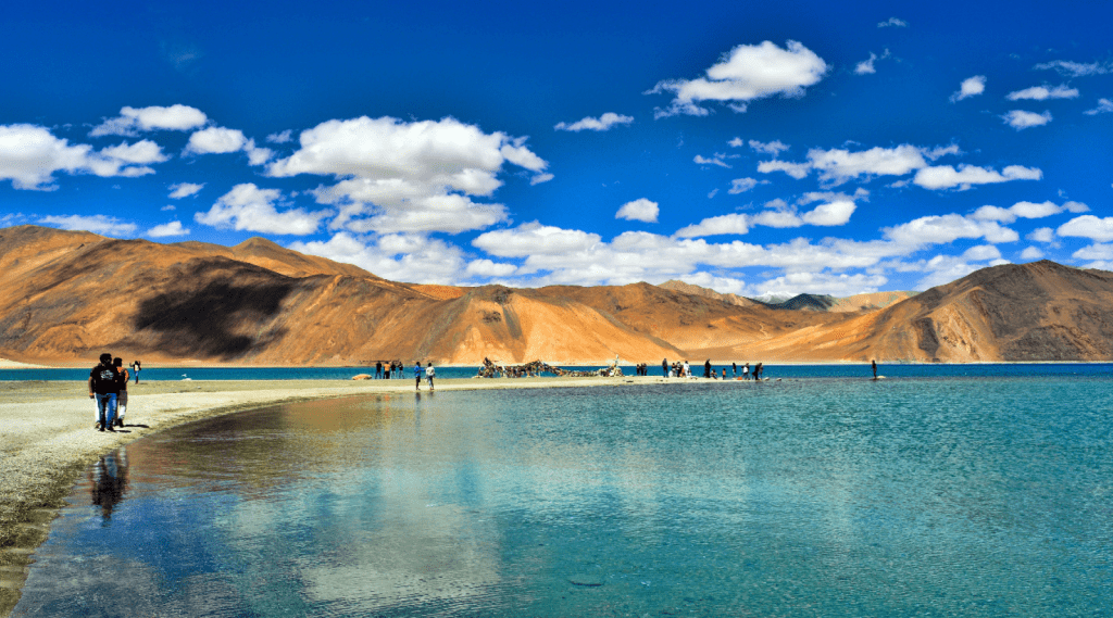 A picturesque scene of people meandering along the shore of a Pangong Tso lake, embracing the serene ambiance of nature.