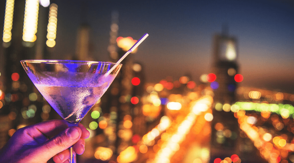 A person holding a martini glass with a cityscape in the background, creating a sophisticated and urban ambiance.