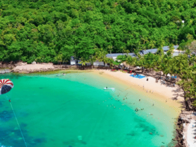 Aerial view of a tropical island featuring a sandy beach and a small boat anchored in clear blue waters.