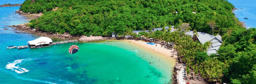 Aerial view of a tropical island featuring a sandy beach and a small boat anchored in clear blue waters.