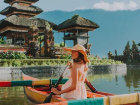 Woman paddling a painted wooden boat on Lake Beratan in front of the tiered shrines of Ulun Danu Beratan temple