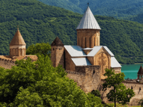 A majestic castle perched on a hill overlooks a serene lake, surrounded by lush greenery and a clear blue sky.