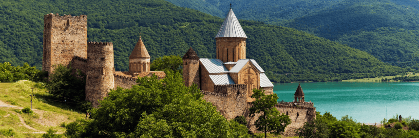 A majestic castle perched on a hill overlooks a serene lake, surrounded by lush greenery and a clear blue sky.