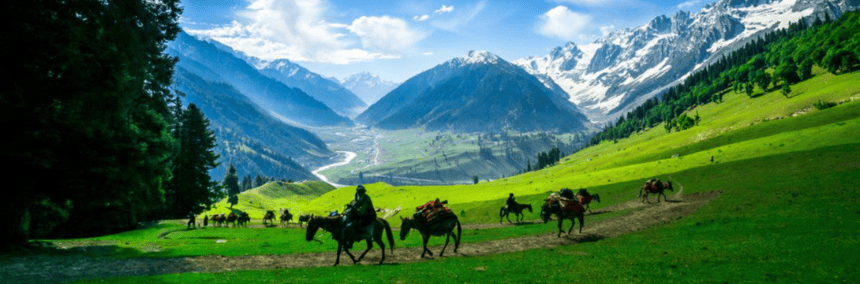 People riding horses through a lush green valley under a clear blue sky.