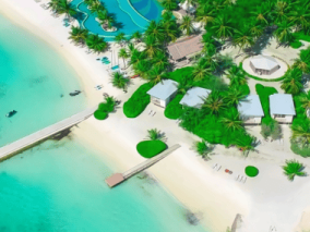 Aerial view of a tropical island featuring white buildings surrounded by lush greenery and clear blue waters.