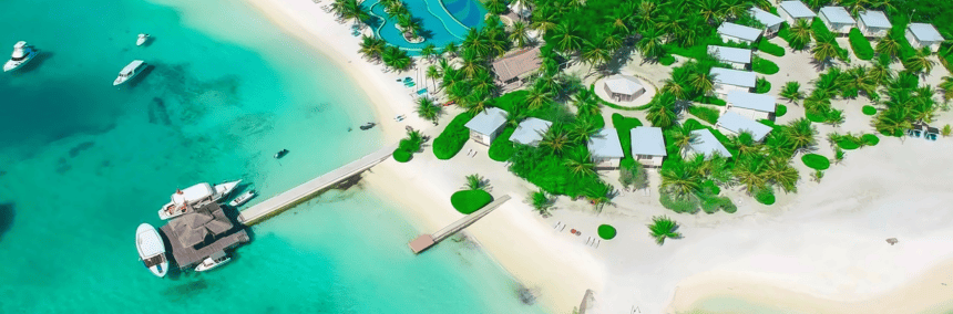 Aerial view of a tropical island featuring white buildings surrounded by lush greenery and clear blue waters.