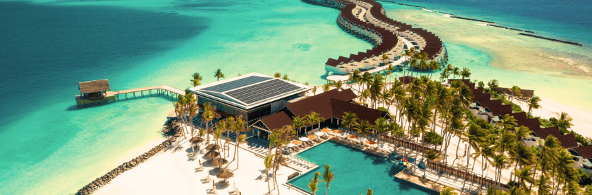 A beach resort featuring a long wooden pier extending into the ocean under a clear blue sky.