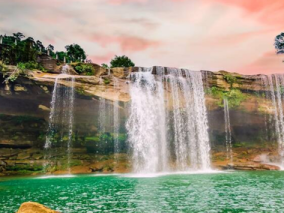 Serene waterfall cascading down rocks in Meghalaya, surrounded by lush greenery and vibrant tropical plants.