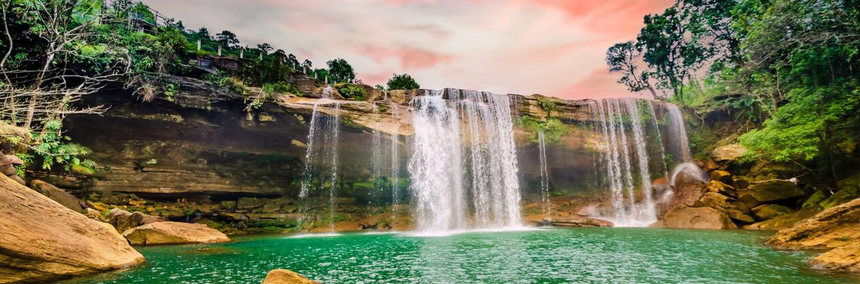 Serene waterfall cascading down rocks in Meghalaya, surrounded by lush greenery and vibrant tropical plants.