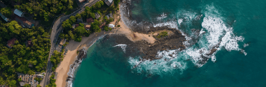 Aerial view showcasing a beach bordered by a lush green forest, highlighting the contrast between land and water.
