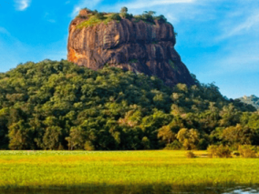 A man and woman are sitting on the elephant in the water, with a majestic mountain in the background, highlighting a peaceful outdoor scene.