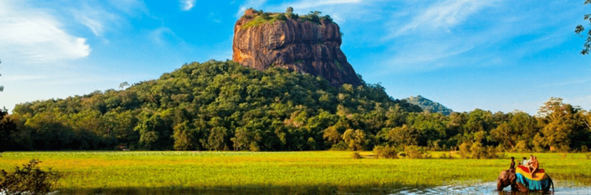 A man and woman are sitting on the elephant in the water, with a majestic mountain in the background, highlighting a peaceful outdoor scene.