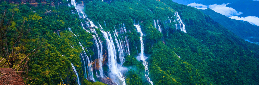A cascading waterfall flows down a rocky mountain, surrounded by lush greenery and steep cliffs.